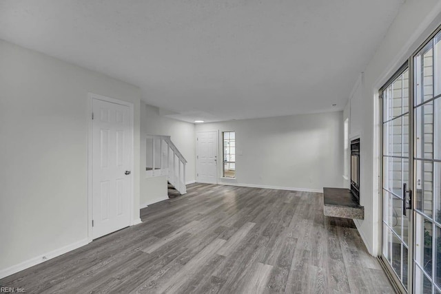 unfurnished living room with stairway, baseboards, and wood finished floors