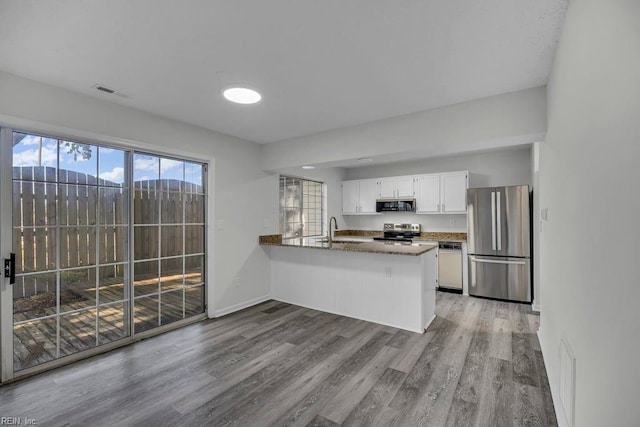 kitchen featuring visible vents, appliances with stainless steel finishes, a peninsula, wood finished floors, and white cabinets