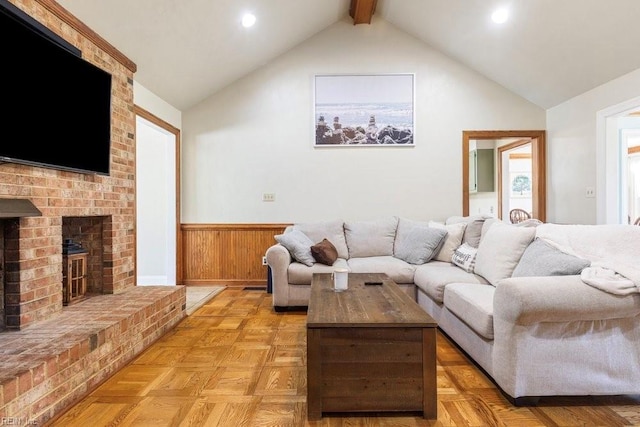 living area with beam ceiling, a brick fireplace, a wainscoted wall, and high vaulted ceiling