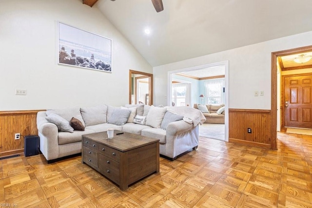 living area with a wainscoted wall, beam ceiling, high vaulted ceiling, wooden walls, and ceiling fan