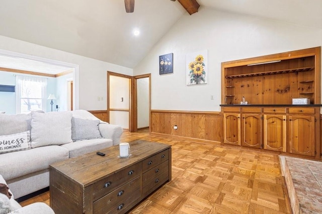 living area with a wainscoted wall, beam ceiling, high vaulted ceiling, and ceiling fan