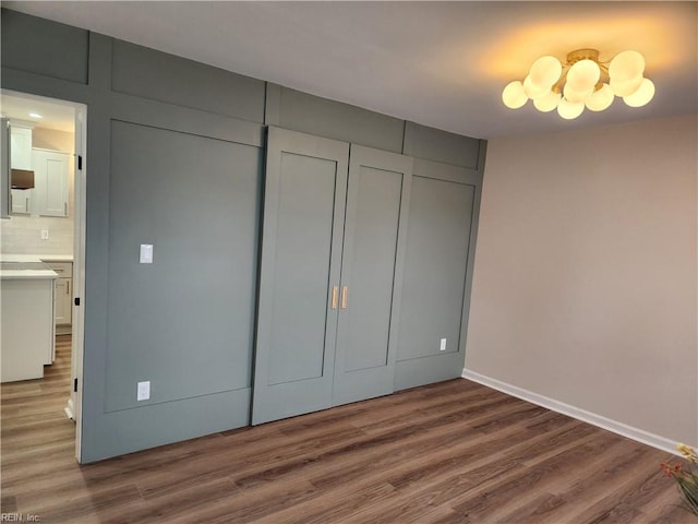 unfurnished bedroom with a chandelier, baseboards, a closet, and wood finished floors