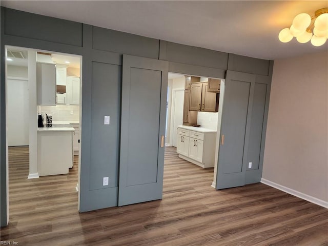 kitchen with a notable chandelier, wood finished floors, light countertops, decorative backsplash, and baseboards