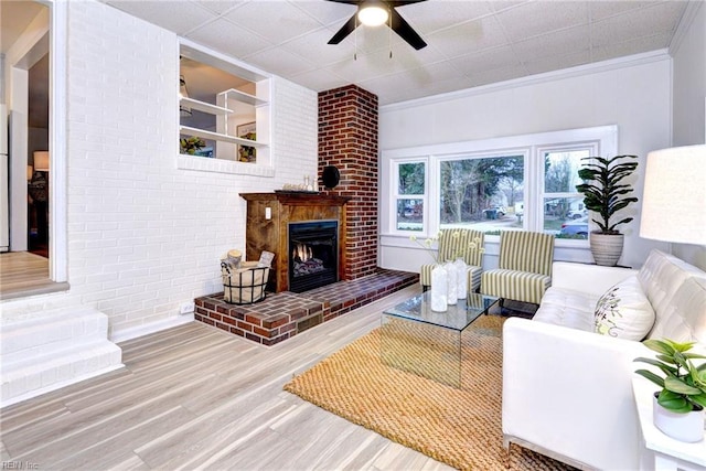 living room with wood finished floors, a fireplace, brick wall, and ceiling fan