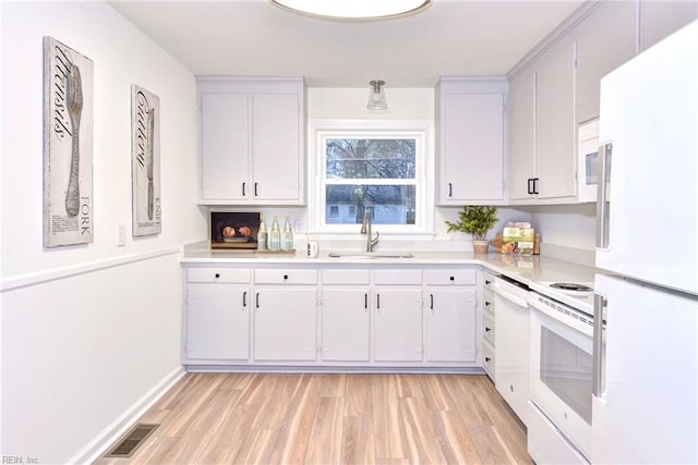 kitchen featuring visible vents, a sink, white appliances, light wood finished floors, and light countertops