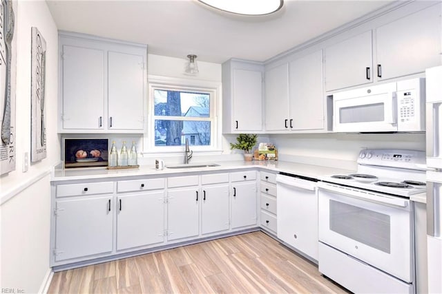 kitchen featuring light wood-type flooring, a sink, white appliances, white cabinets, and light countertops