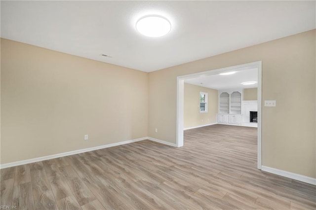 empty room with built in shelves, light wood-style floors, baseboards, and a fireplace with raised hearth