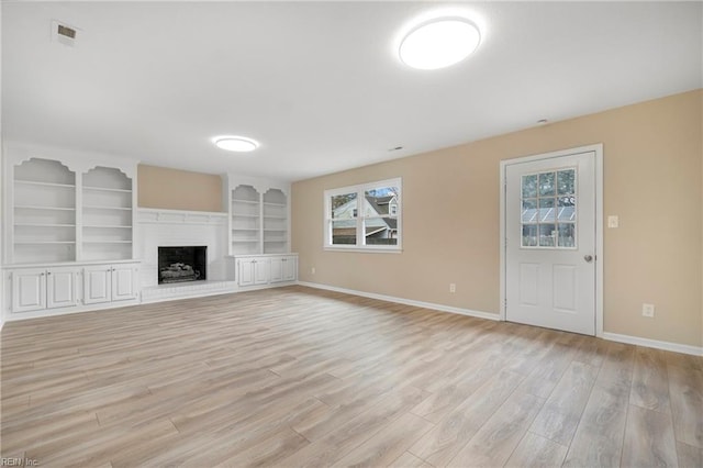 unfurnished living room with light wood-type flooring, visible vents, built in shelves, a fireplace, and baseboards