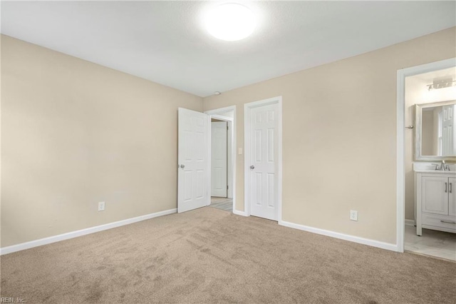 unfurnished bedroom featuring connected bathroom, baseboards, carpet floors, and a sink