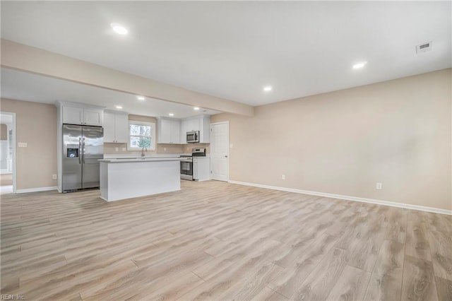 kitchen featuring light wood finished floors, a center island, open floor plan, stainless steel appliances, and white cabinetry