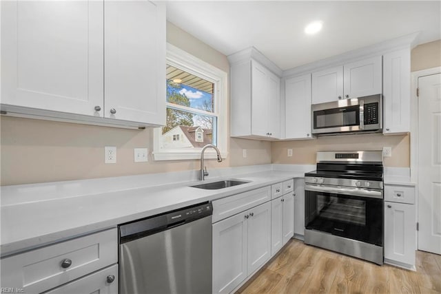 kitchen featuring a sink, light countertops, light wood-style floors, appliances with stainless steel finishes, and white cabinetry