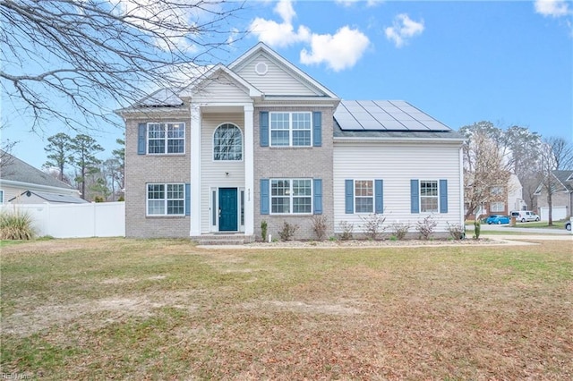 view of front facade featuring brick siding, solar panels, a front lawn, and fence