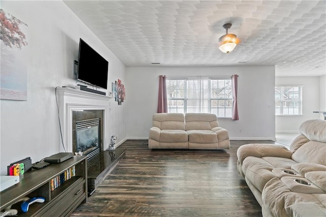 living area featuring dark wood-style floors, baseboards, and a glass covered fireplace