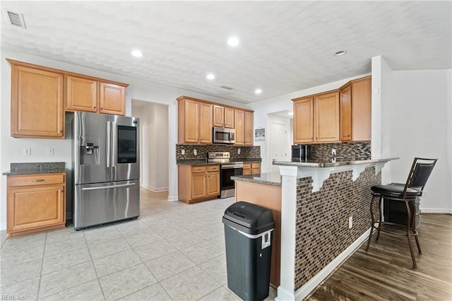 kitchen with visible vents, backsplash, a breakfast bar area, a peninsula, and stainless steel appliances