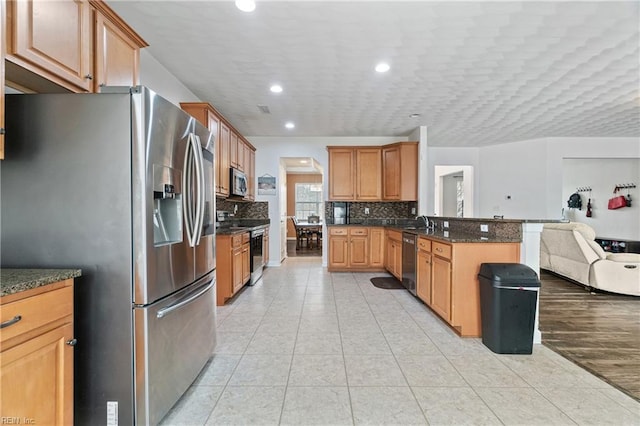 kitchen with light tile patterned floors, a peninsula, decorative backsplash, appliances with stainless steel finishes, and open floor plan