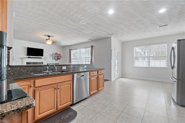 kitchen featuring dark stone counters, light tile patterned floors, brown cabinets, appliances with stainless steel finishes, and a sink