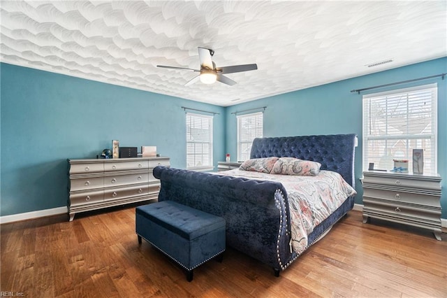 bedroom with ceiling fan, a textured ceiling, baseboards, and wood finished floors