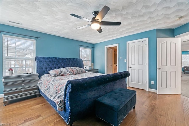 bedroom with visible vents, a textured ceiling, wood finished floors, baseboards, and ceiling fan