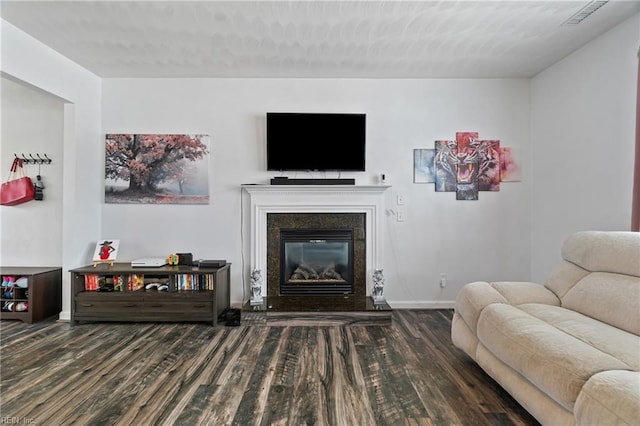 living room featuring a glass covered fireplace, visible vents, baseboards, and wood finished floors