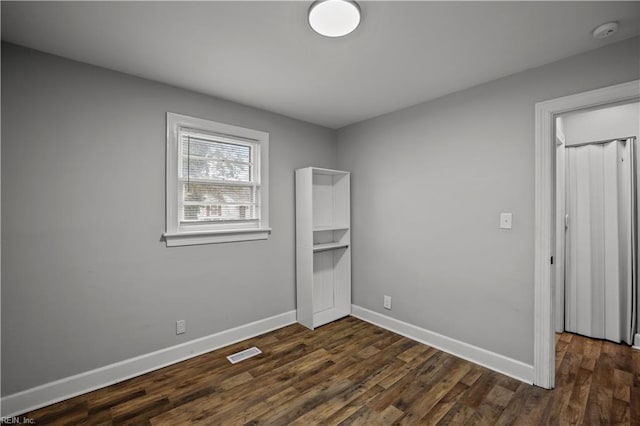 unfurnished room with visible vents, baseboards, and dark wood-style floors