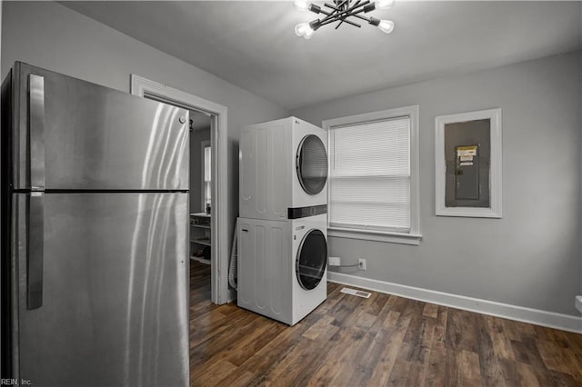 washroom featuring dark wood-style floors, baseboards, stacked washing maching and dryer, electric panel, and a notable chandelier