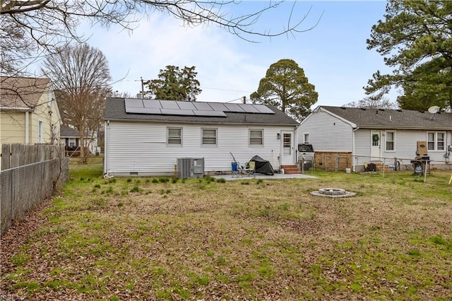 rear view of house with entry steps, an outdoor fire pit, roof mounted solar panels, a yard, and a fenced backyard