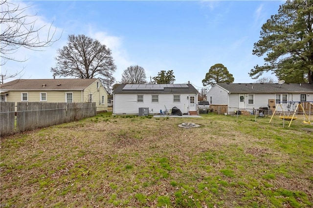 back of property featuring central air condition unit, a lawn, a fenced backyard, an outdoor fire pit, and solar panels