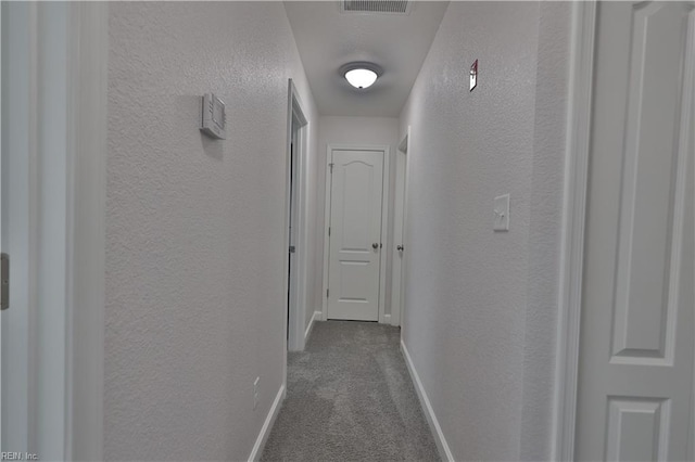 corridor featuring visible vents, baseboards, dark carpet, and a textured wall