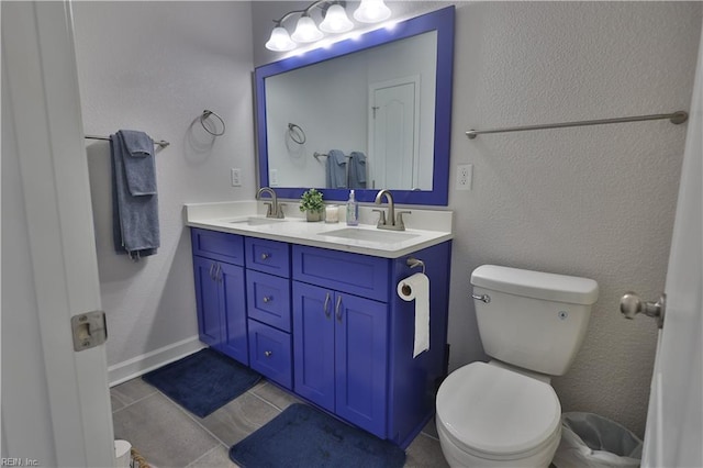 bathroom featuring double vanity, toilet, a textured wall, and a sink