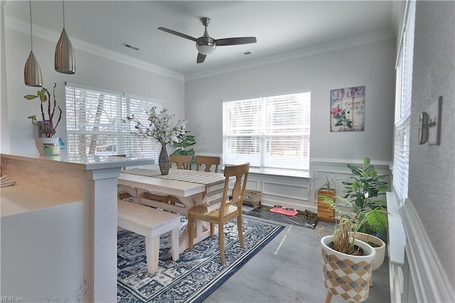 dining space featuring visible vents, crown molding, a wainscoted wall, a decorative wall, and a ceiling fan