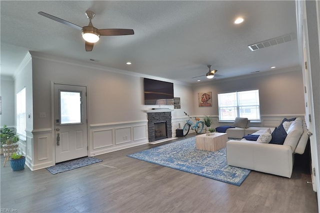 living room with visible vents, wood finished floors, a fireplace, wainscoting, and ceiling fan