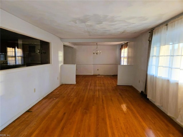 empty room featuring an inviting chandelier, wood finished floors, and baseboards