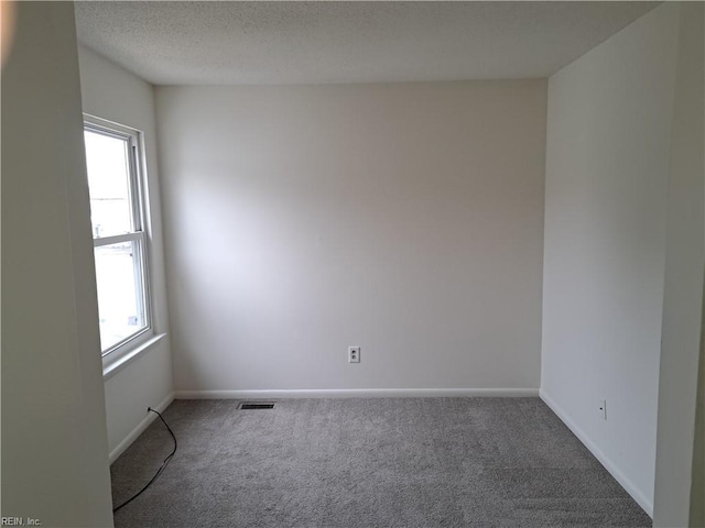 carpeted spare room featuring visible vents, baseboards, and a textured ceiling