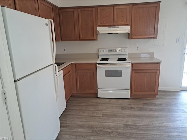 kitchen with under cabinet range hood, white appliances, light countertops, and light wood-style floors