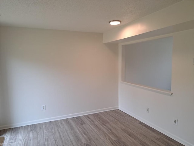 empty room featuring a textured ceiling, baseboards, and wood finished floors