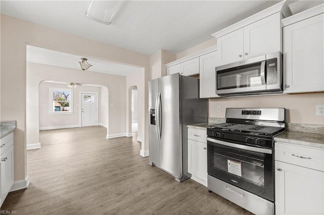 kitchen featuring baseboards, light wood finished floors, arched walkways, appliances with stainless steel finishes, and white cabinetry