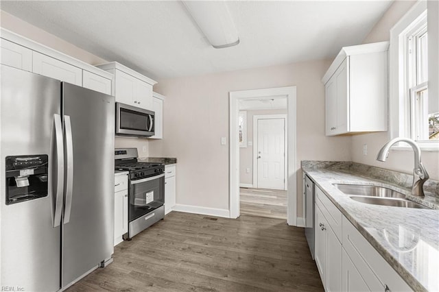 kitchen with a sink, appliances with stainless steel finishes, wood finished floors, and white cabinets