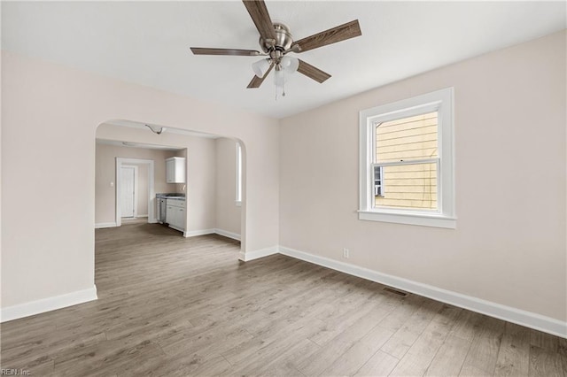 unfurnished room with arched walkways, visible vents, ceiling fan, and wood finished floors