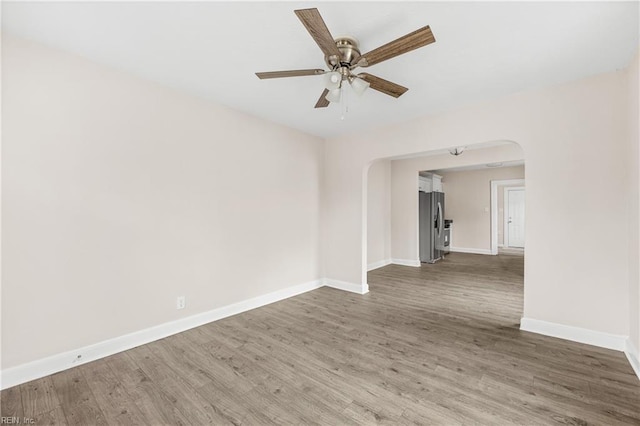 unfurnished room with arched walkways, baseboards, a ceiling fan, and wood finished floors