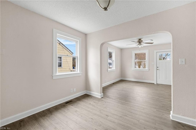 unfurnished room with wood finished floors, visible vents, arched walkways, and a textured ceiling