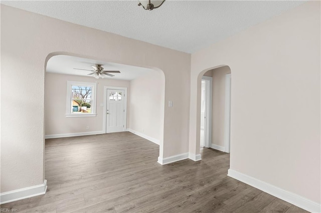 interior space featuring ceiling fan, baseboards, arched walkways, and wood finished floors