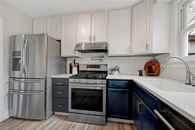 kitchen featuring under cabinet range hood, blue cabinetry, a sink, appliances with stainless steel finishes, and light countertops