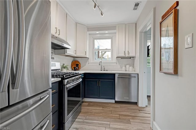 kitchen with under cabinet range hood, light countertops, appliances with stainless steel finishes, white cabinets, and a sink