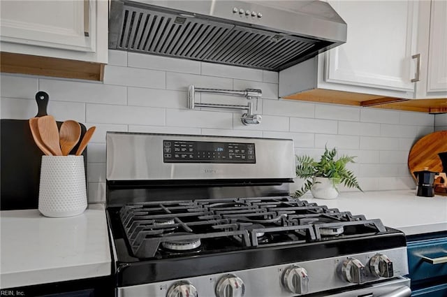 interior details with backsplash, white cabinets, light countertops, extractor fan, and stainless steel gas range