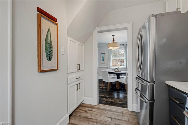 kitchen featuring baseboards, light countertops, freestanding refrigerator, light wood-style floors, and white cabinetry