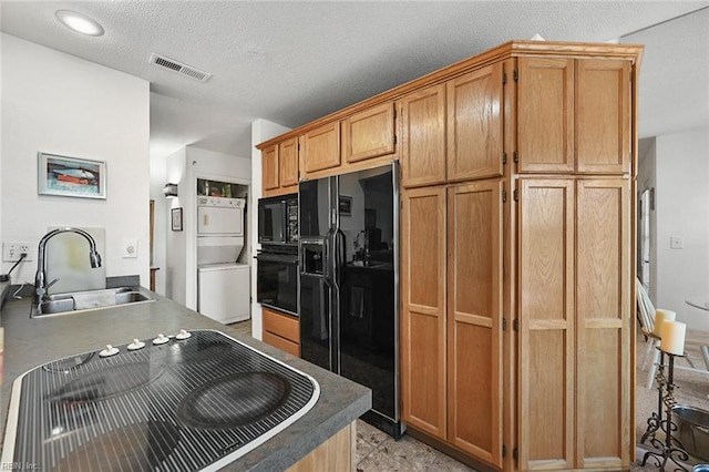 kitchen featuring visible vents, stacked washer and dryer, black appliances, a sink, and dark countertops