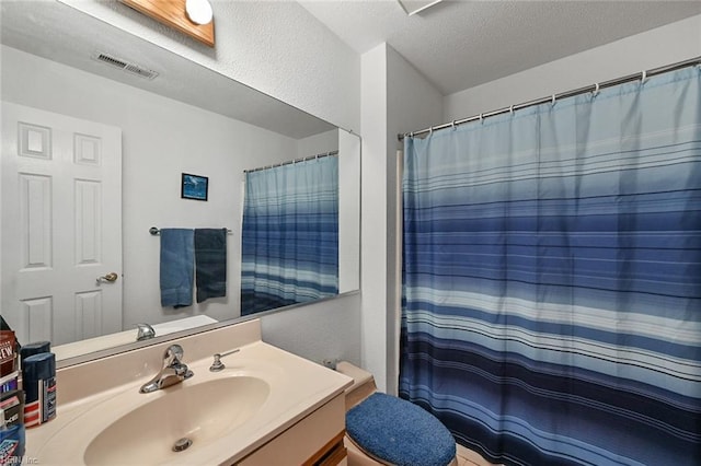 bathroom with vanity, visible vents, a textured ceiling, toilet, and a textured wall