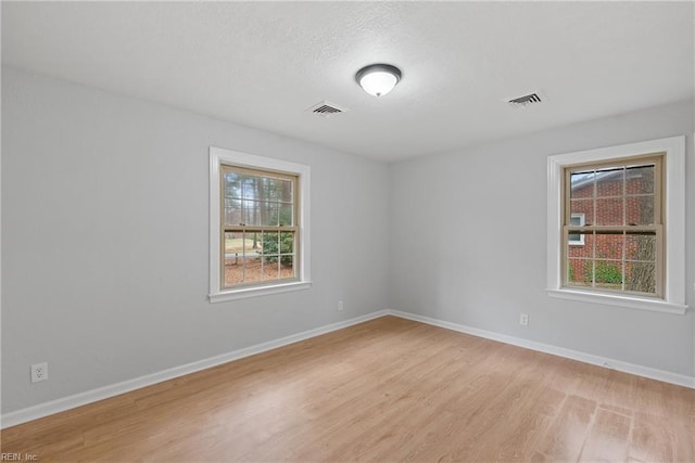 spare room with a textured ceiling, baseboards, visible vents, and light wood-type flooring