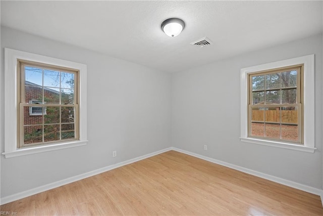 unfurnished room featuring light wood-type flooring, visible vents, baseboards, and a healthy amount of sunlight