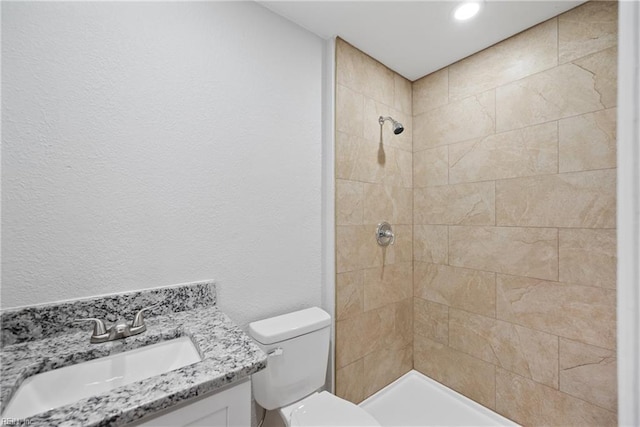 bathroom with a tile shower, toilet, and vanity